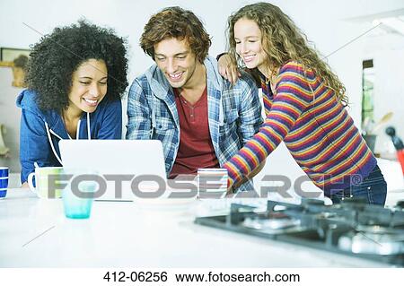 Friends using laptop together in kitchen View Large Photo Image Stock Photograph - Friends using laptop together in kitchen. Fotosearch
