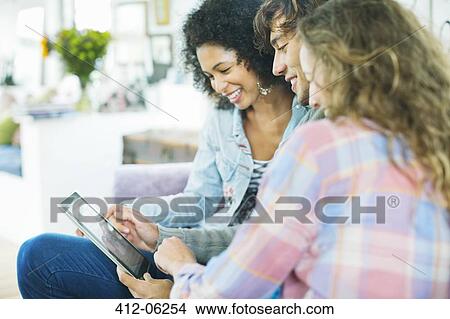 Friends using tablet computer on sofa View Large Photo Image Picture - Friends using tablet computer on sofa. Fotosearch