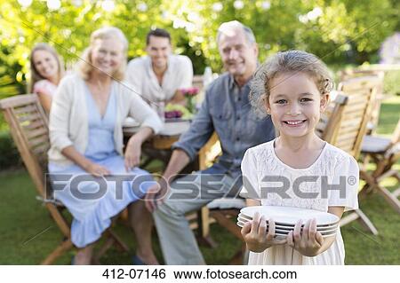 Stock Photograph - Girl carrying plates to table outdoors. Fotosearch