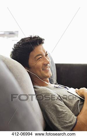 Man listening to headphones on sofa View Large Photo Image Picture - Man listening to headphones on sofa. Fotosearch