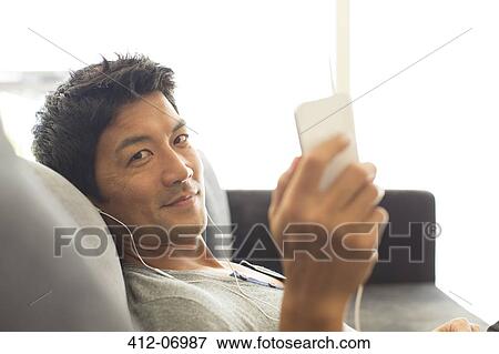 Man listening to headphones on sofa View Large Photo Image Stock Photo - Man listening to headphones on sofa. Fotosearch