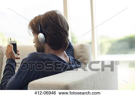 Man listening to headphones on sofa View Large Photo Image Stock Photograph - Man listening to headphones on sofa. Fotosearch