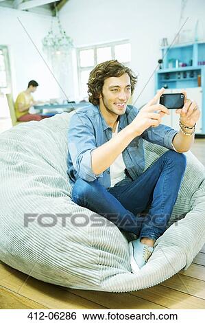 Man using cell phone in beanbag chair View Large Photo Image Stock Photograph - Man using cell phone in beanbag chair. Fotosearch