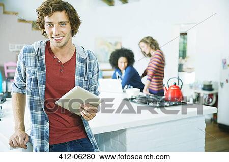 Stock Image - Man using tablet computer in kitchen. Fotosearch