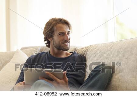 Stock Image - Man using tablet computer on sofa. Fotosearch