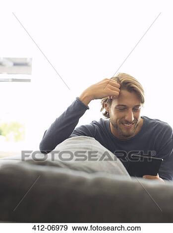 Stock Photo - Man using tablet computer on sofa. Fotosearch