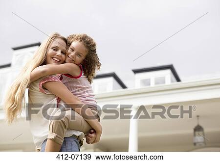 Stock Photo - Mother and daughter hugging outside house. Fotosearch