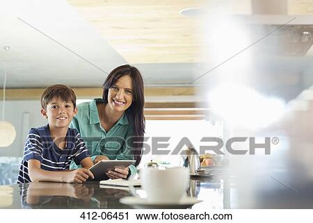 Stock Image - Mother and son using tablet computer in kitchen. Fotosearch