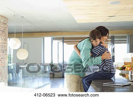 Stock Image - Mother hugging son in kitchen. Fotosearch