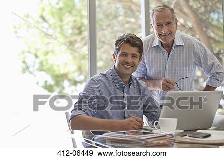 Older man and younger man smiling together at desk View Large Photo Image Stock Photo - Older man and younger man smiling together at desk. Fotosearch