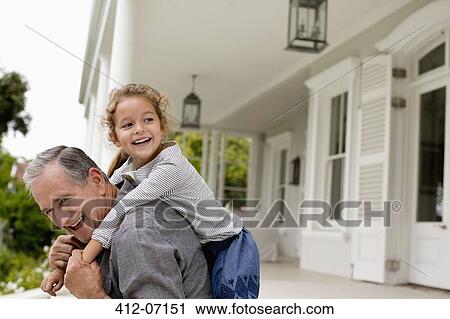 Stock Image - Older man carrying granddaughter piggy back on porch. Fotosearch