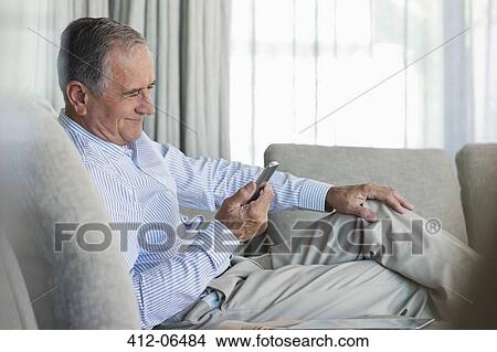 Older man using cell phone on sofa View Large Photo Image Picture - Older man using cell phone on sofa. Fotosearch