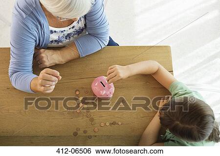 Stock Photograph - Older woman and granddaughter filling piggy bank. Fotosearch