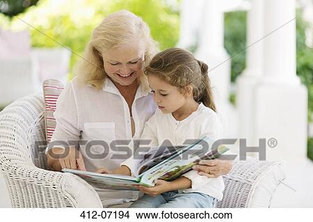 Picture - Older woman reading to granddaughter on porch. Fotosearch