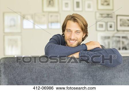 Smiling man sitting on sofa View Large Photo Image Stock Photograph - Smiling man sitting on sofa. Fotosearch