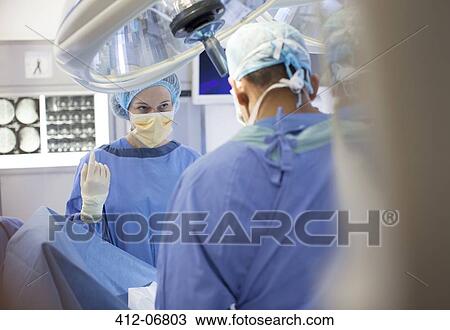 Stock Image - Surgeons standing over patient in operating room. Fotosearch