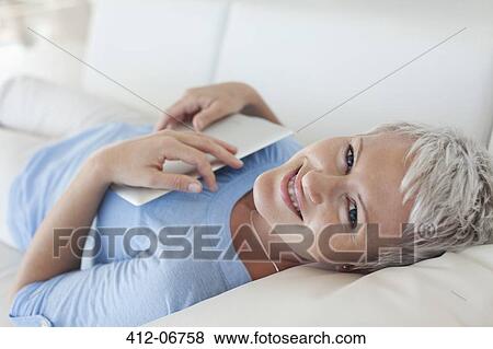 Woman holding tablet computer on sofa View Large Photo Image Stock Photo - Woman holding tablet computer on sofa. Fotosearch