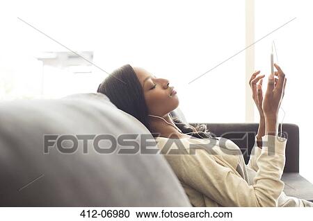 Stock Image - Woman listening to headphones on sofa. Fotosearch
