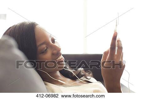Stock Image - Woman listening to headphones on sofa. Fotosearch