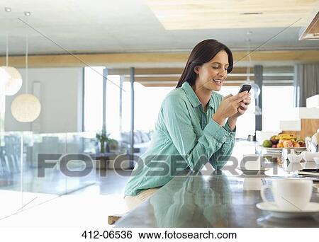 Woman using cell phone in kitchen View Large Photo Image Stock Photograph - Woman using cell phone in kitchen. Fotosearch