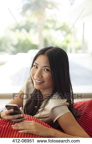 Stock Image - Woman using cell phone on sofa. Fotosearch