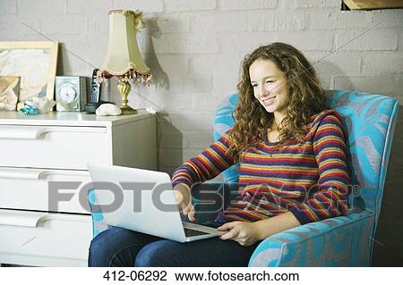 Stock Image - Woman using laptop in armchair. Fotosearch