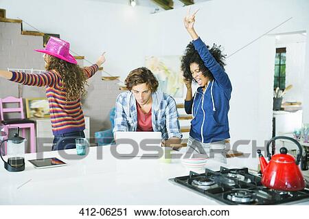 Stock Image - Women dancing around man in kitchen. Fotosearch