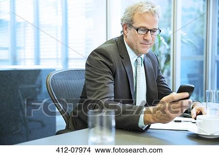 Businessman text messaging with cell phone in conference room View Large Photo Image Picture - Businessman text messaging with cell phone in conference room. Fotosearch