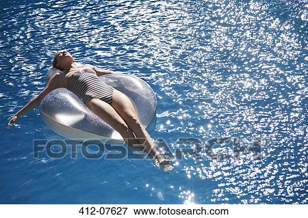 Stock Photo - Carefree woman floating on inflatable ring in swimming pool. Fotosearch