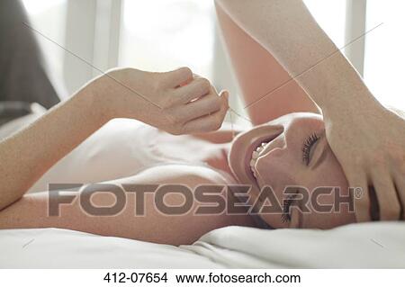 Picture - Close up of smiling woman laying in bed with head in hands. Fotosearch