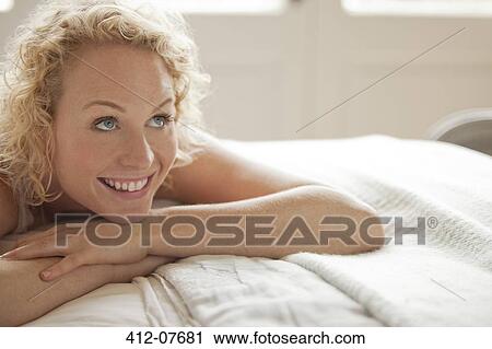 Stock Image - Enthusiastic woman laying in bed and looking up. Fotosearch