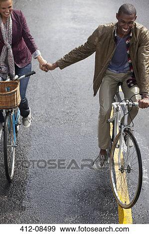 Stock Photo - Happy couple holding hands and riding bicycles. Fotosearch