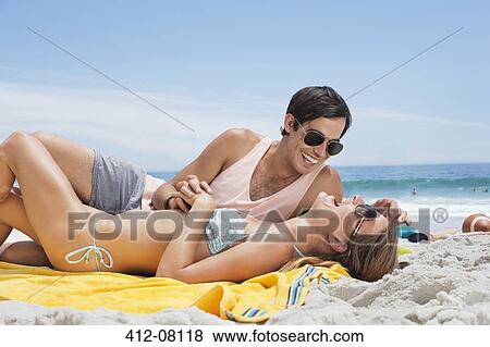 Stock Photo - Happy couple laying on blanket at beach. Fotosearch