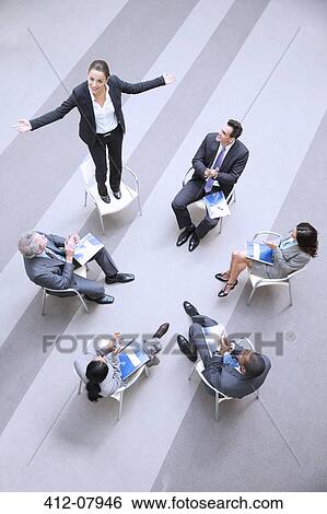 High angle view of businesswoman standing on chair in circle with co-workers View Large Photo Image Stock Photograph - High angle view of businesswoman standing on chair in circle with co-workers. Fotosearch