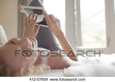 Stock Photo - Laughing woman laying in bed using digital tablet. Fotosearch