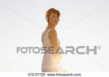 Pensive woman in dress wearing headphones and looking back View Large Photo Image Stock Image - Pensive woman in dress wearing headphones and looking back. Fotosearch