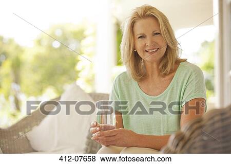 Stock Photo - Portrait of smiling woman drinking water on patio. Fotosearch