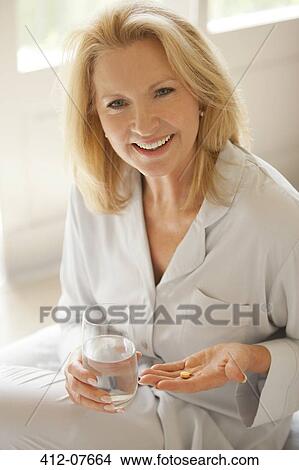 Picture - Portrait of smiling woman holding pill and glass of water. Fotosearch