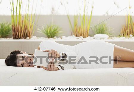 Portrait of smiling woman laying on patio sofa using digital tablet View Large Photo Image Stock Photograph - Portrait of smiling woman laying on patio sofa using digital tablet. Fotosearch