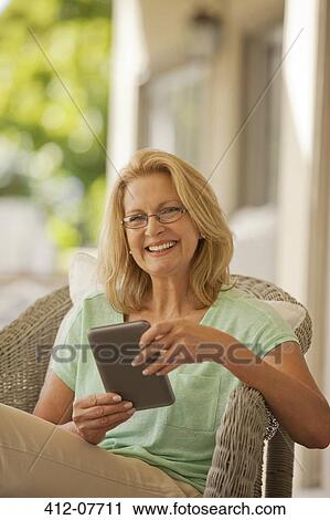 Stock Image - Portrait of smiling woman using digital tablet on porch. Fotosearch