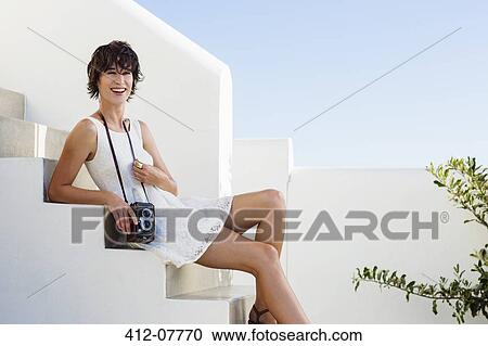 Stock Image - Portrait of smiling woman with vintage camera on stairs. Fotosearch