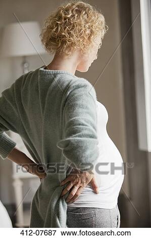 Stock Photo - Pregnant woman holding back in pain. Fotosearch