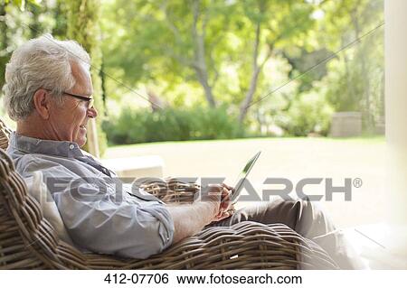 Senior man using digital tablet in wicker armchair on porch View Large Photo Image Stock Photograph - Senior man using digital tablet in wicker armchair on porch. Fotosearch