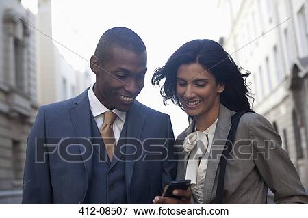 Smiling business people text messaging with cell phone View Large Photo Image Stock Photo - Smiling business people text messaging with cell phone. Fotosearch