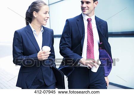 Stock Photography - Smiling businessman and businesswoman walking with coffee. Fotosearch