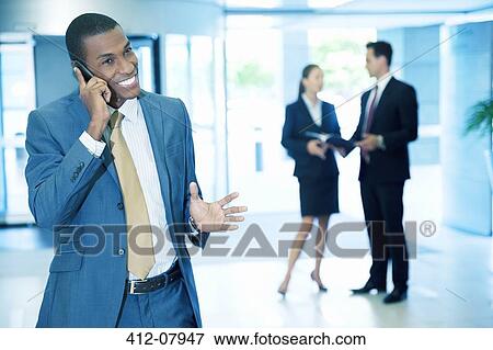 Smiling businessman talking on cell phone and gesturing in lobby View Large Photo Image Stock Photo - Smiling businessman talking on cell phone and gesturing in lobby. Fotosearch