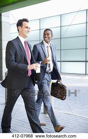 Smiling businessmen walking with coffee View Large Photo Image Stock Photo - Smiling businessmen walking with coffee. Fotosearch