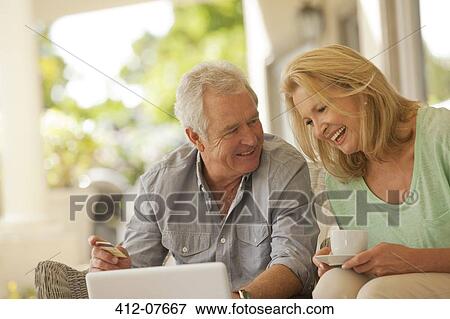 Smiling couple drinking coffee and shopping online on patio View Large Photo Image Stock Photo - Smiling couple drinking coffee and shopping online on patio. Fotosearch