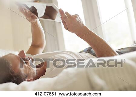 Smiling man laying on bed and using digital tablet View Large Photo Image Stock Image - Smiling man laying on bed and using digital tablet. Fotosearch