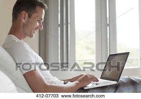 Smiling man using laptop in bed View Large Photo Image Stock Image - Smiling man using laptop in bed. Fotosearch